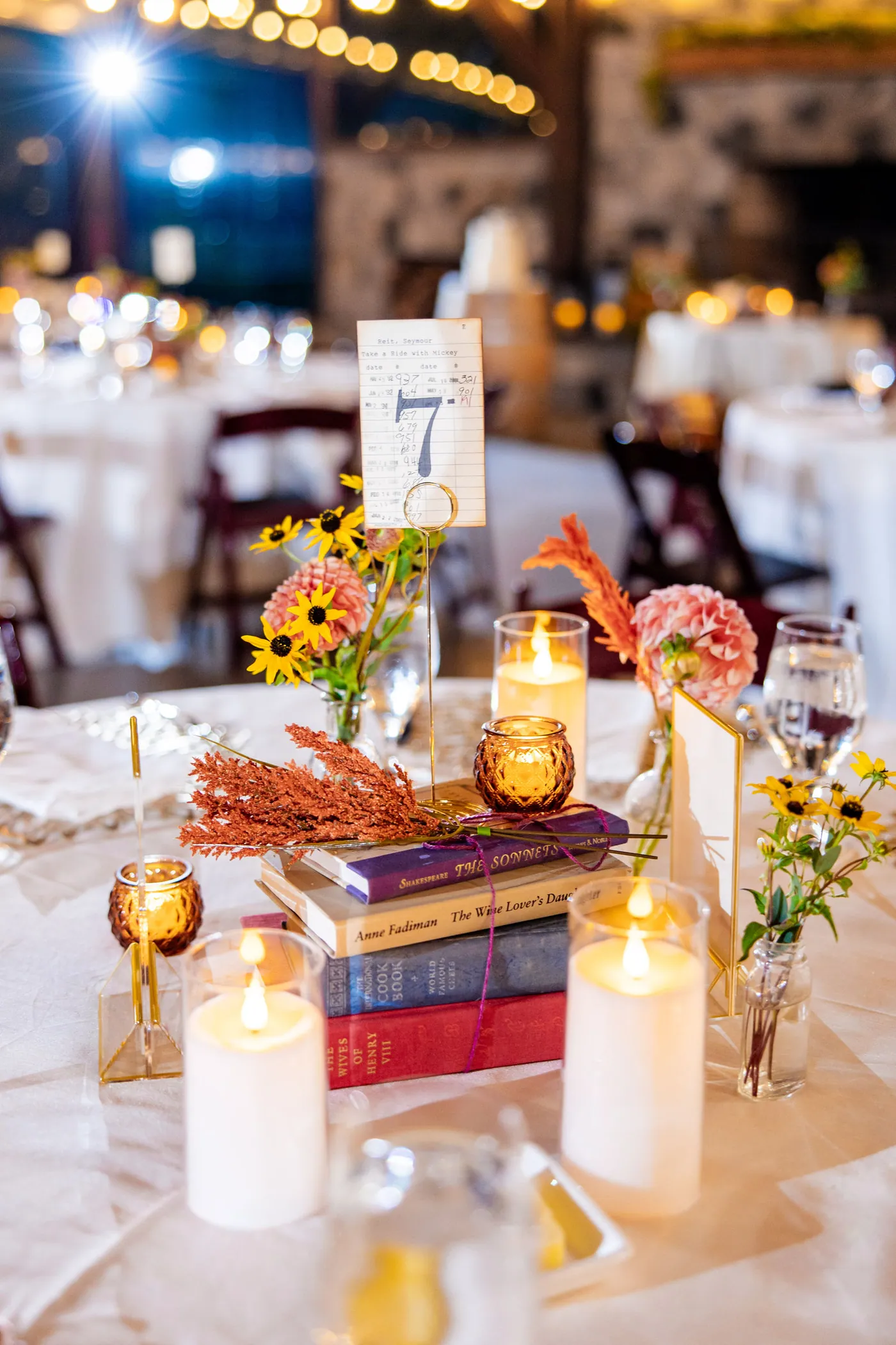 A reception centerpiece of stacked books, candles and sunflowers
